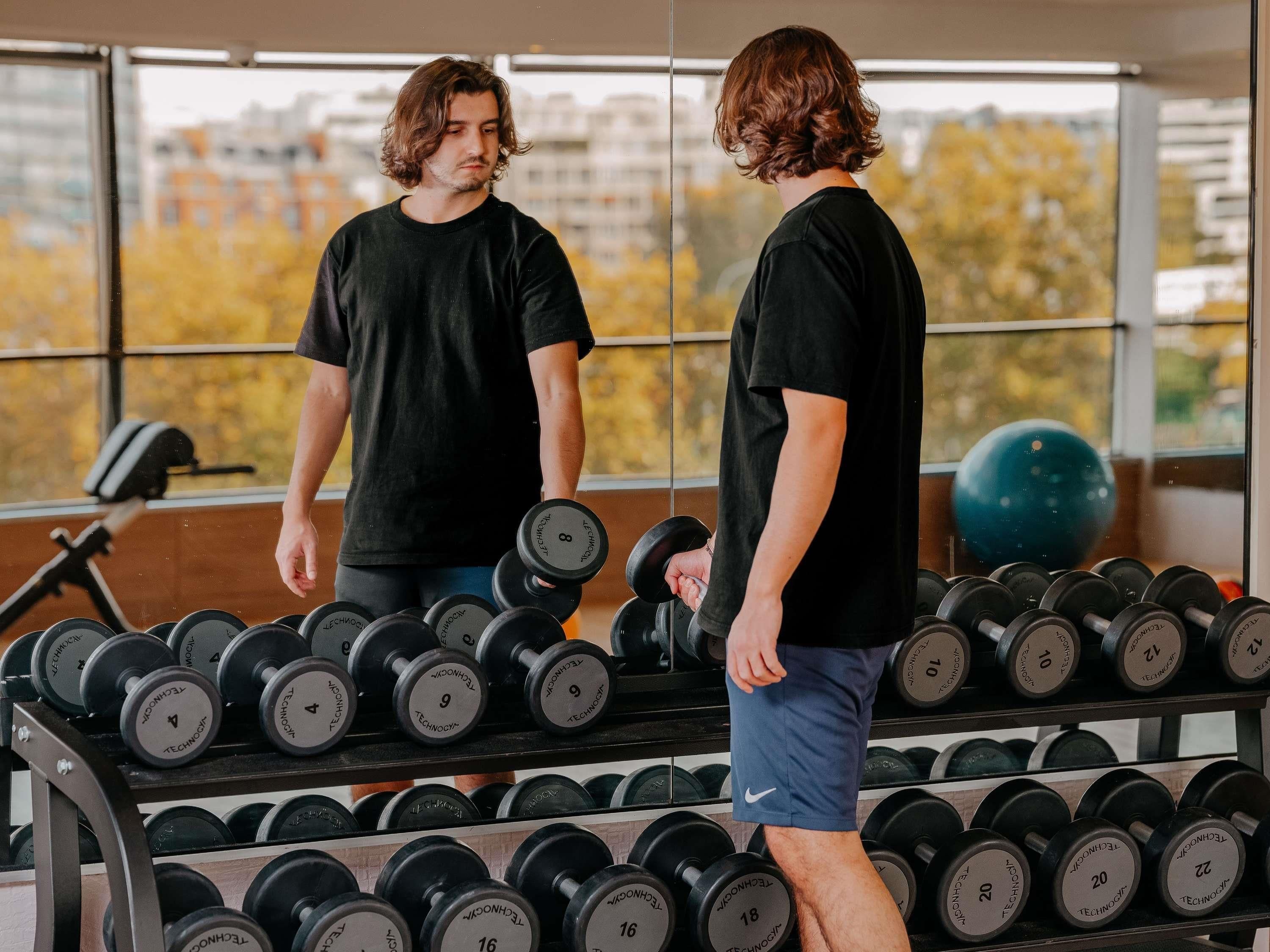 A gym with a person standing in front of a rack of dumbbells.