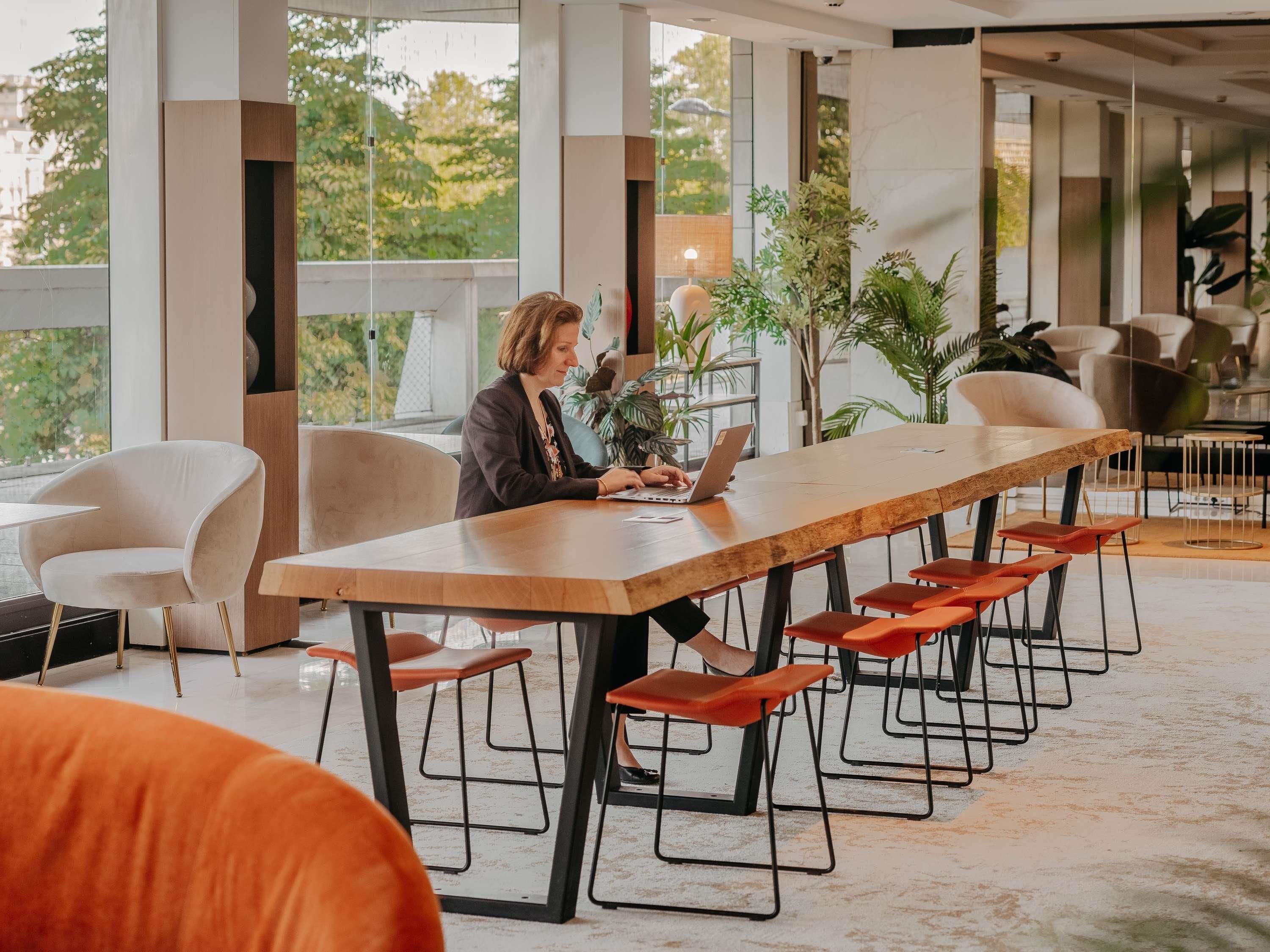 A modern meeting room with a long table, multiple chairs, and large windows.