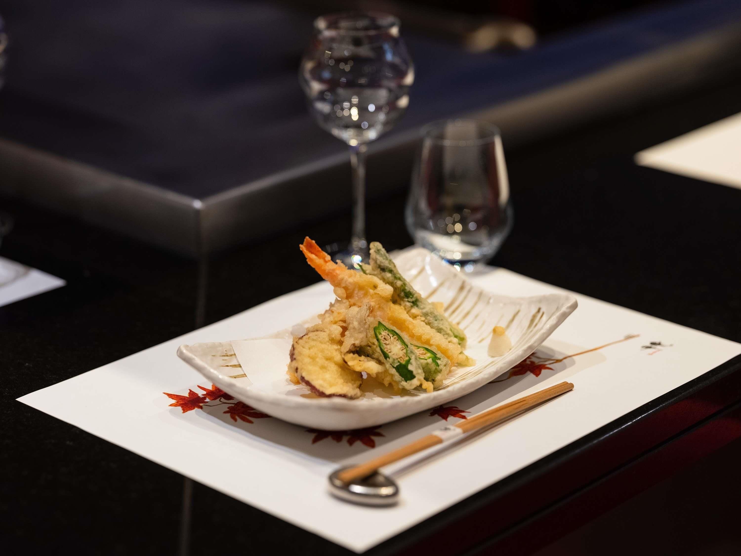 A plate of tempura with a dipping sauce, a pair of chopsticks, and a glass of water on a table.