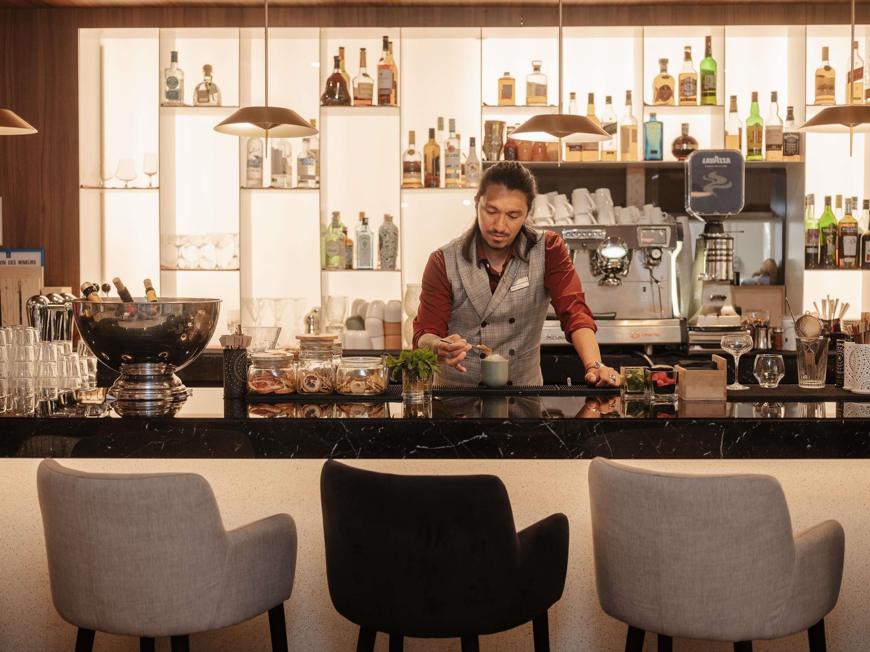 Un espace bar avec un barman préparant des boissons, des étagères remplies de bouteilles et un appareil à café.