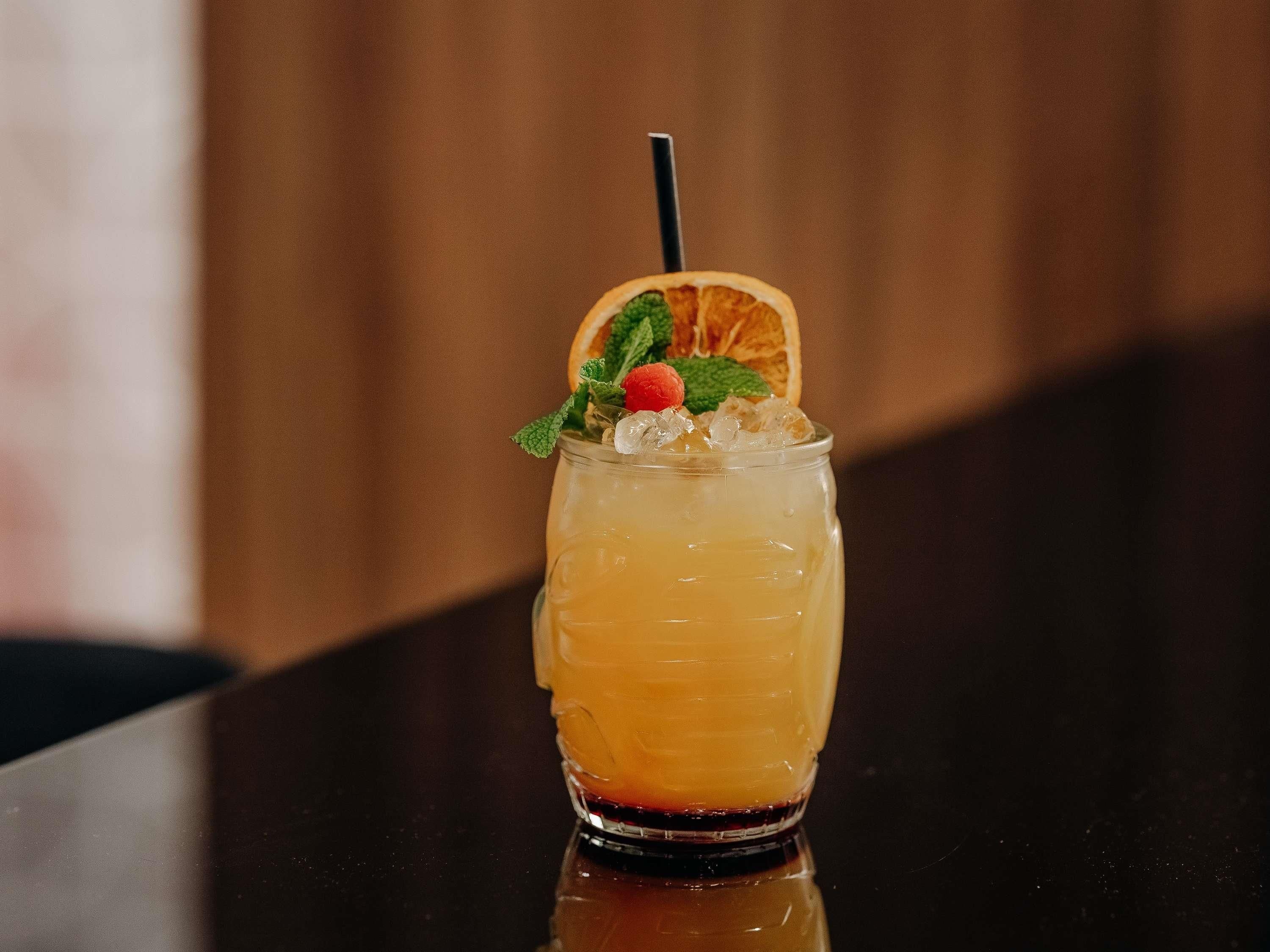 A glass with a layered drink, garnished with mint, a strawberry, and an orange slice, with a straw.