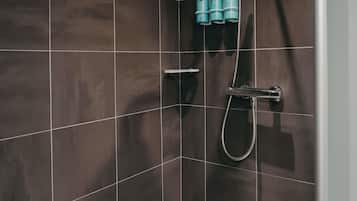 A tiled shower wall with a handheld showerhead and three bottles of shampoo.