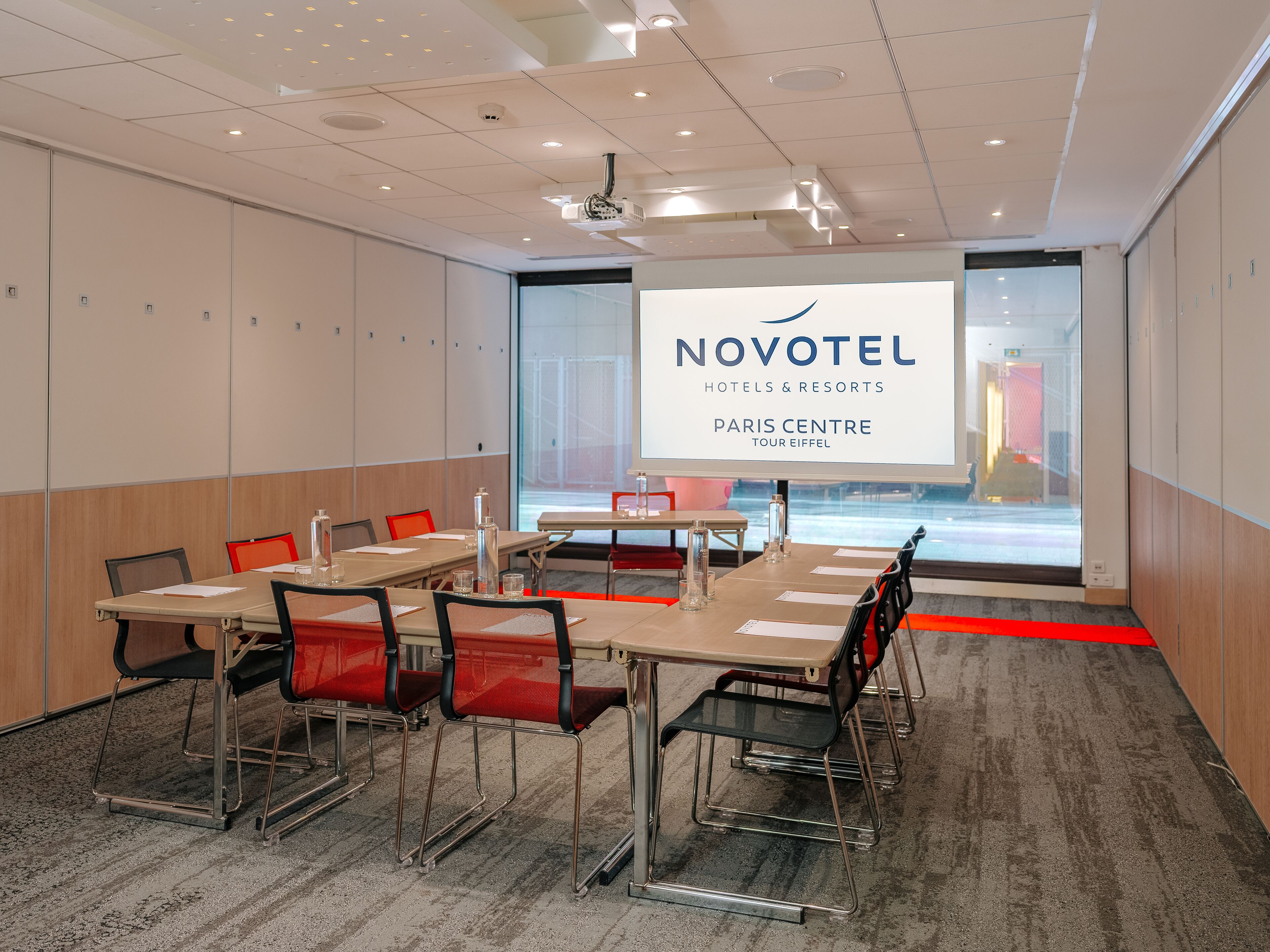 A modern conference room with a large screen displaying 'NOVOTEL HOTELS & RESORTS PARIS CENTRE TOUR EIFFEL'.