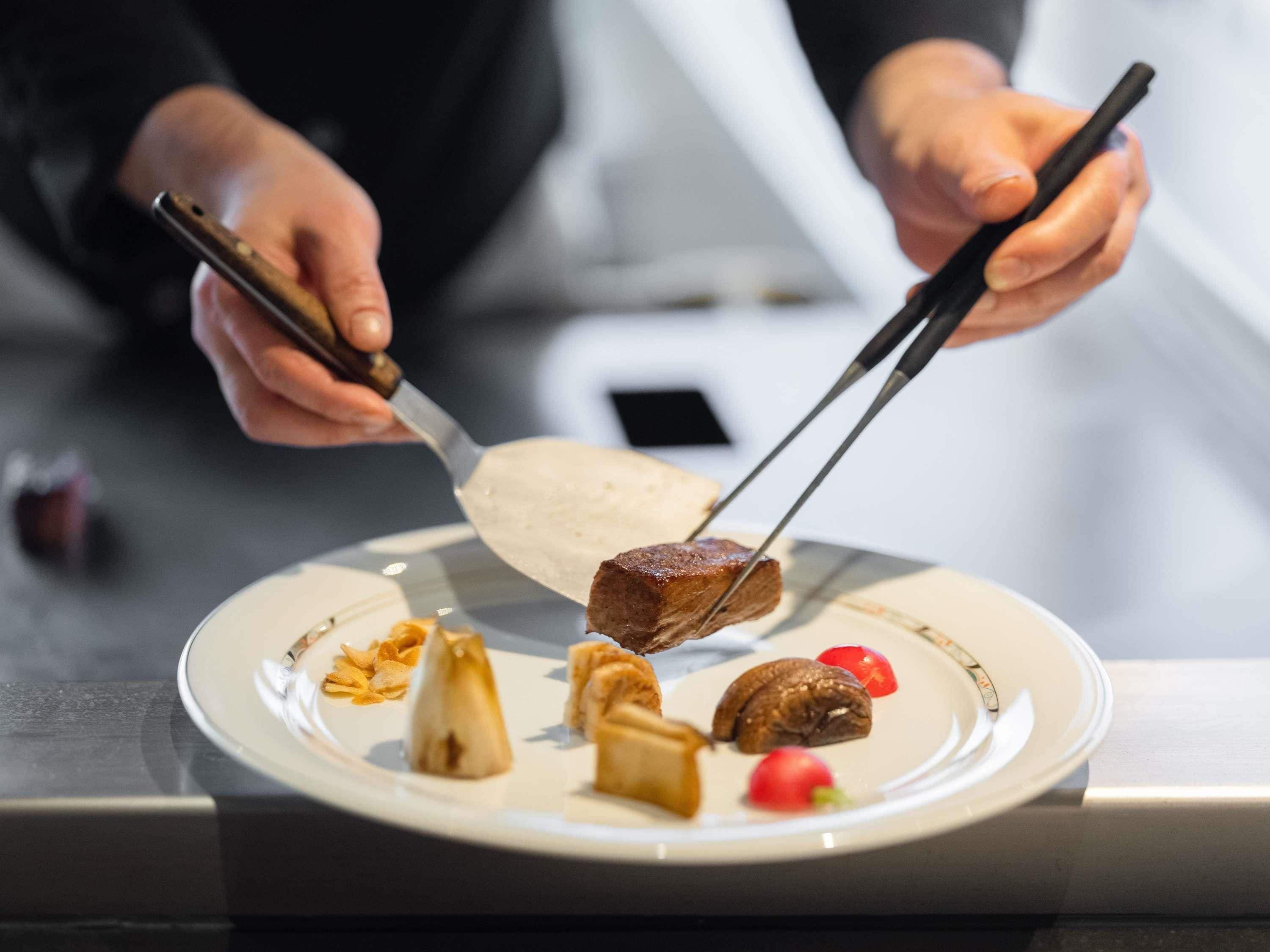 Iemand eet met stokjes een stuk vlees van een bord met diverse bijgerechten.