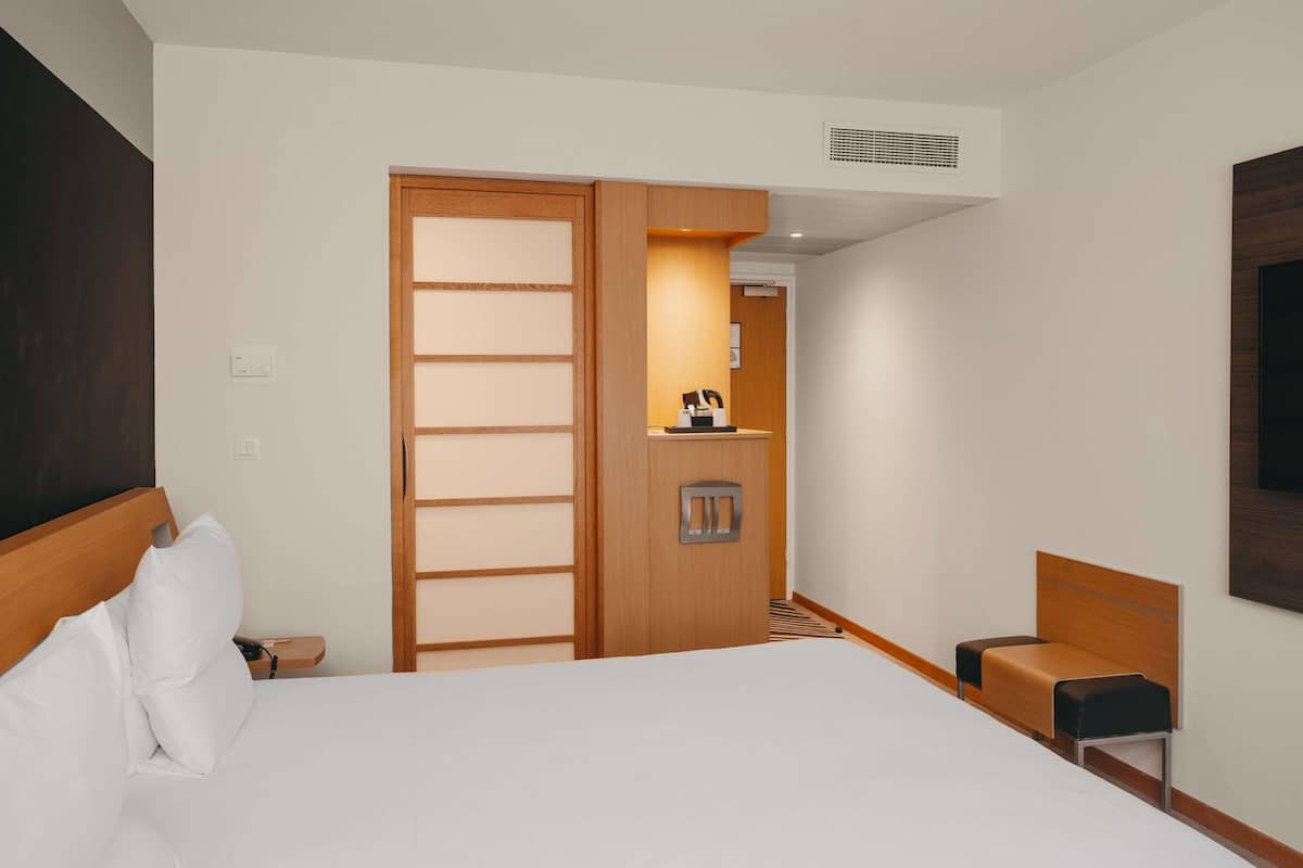 Habitación de hotel con cama, armario de madera, escritorio pequeño con silla y televisor montado en la pared.