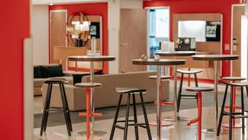 Un interior moderno con mesas y taburetes redondos, un sofá y una zona de cocina al fondo.