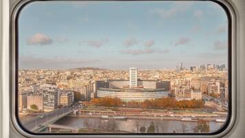 Une vue sur une ville à travers une fenêtre, avec un fleuve, un pont et un mélange de bâtiments modernes et plus anciens.