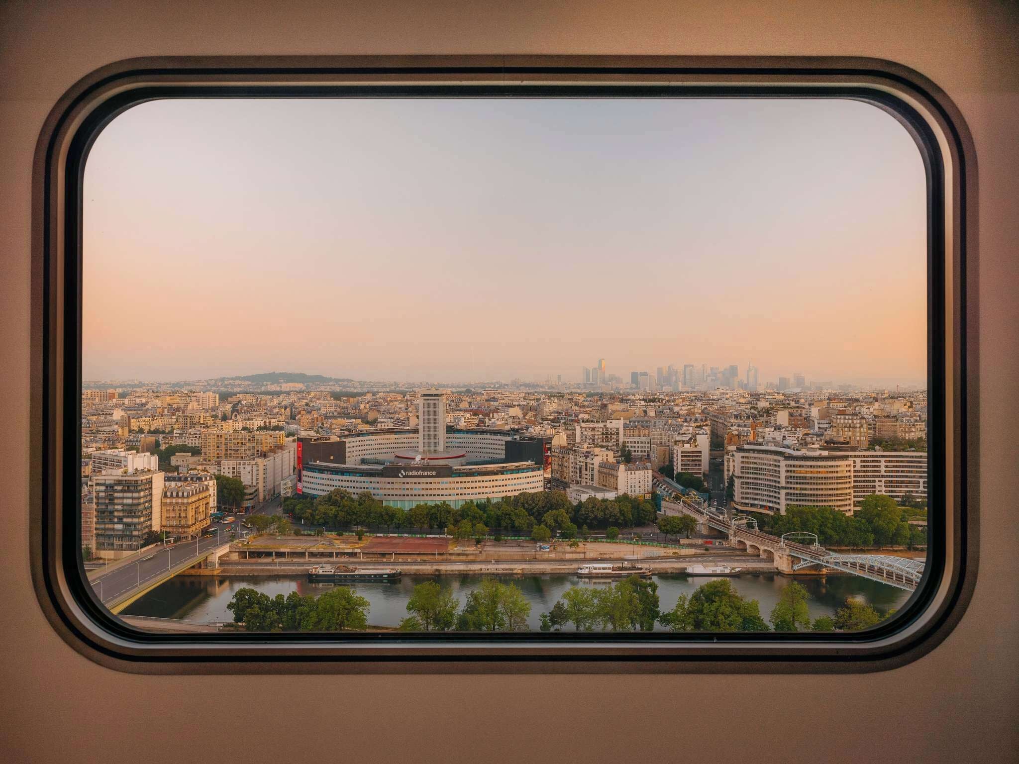 A panoramic view of a cityscape through a window, featuring a prominent building with 'radiofrance' signage, a river, and a bridge.