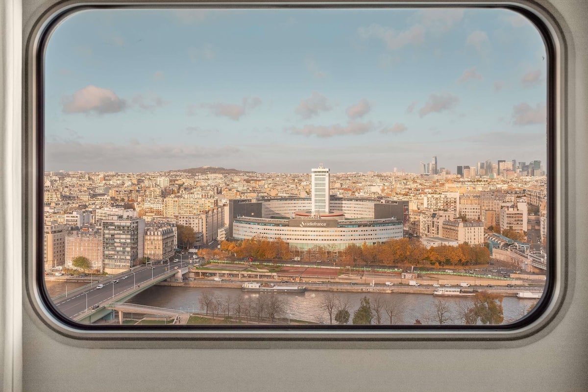 Vista de la ciudad a través de una ventana, con un río, un puente y una combinación de edificios modernos y antiguos.
