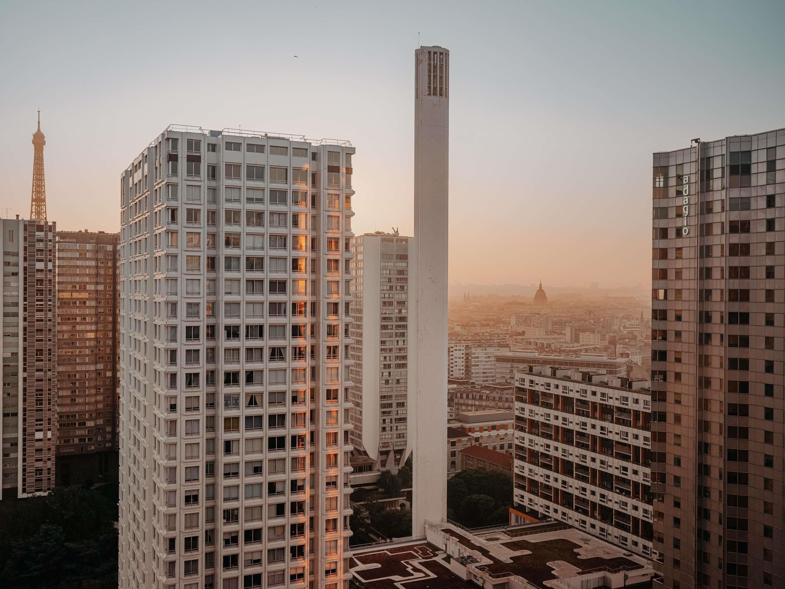 Un edificio alto con una estructura vertical destacada, rodeado de otros edificios residenciales.