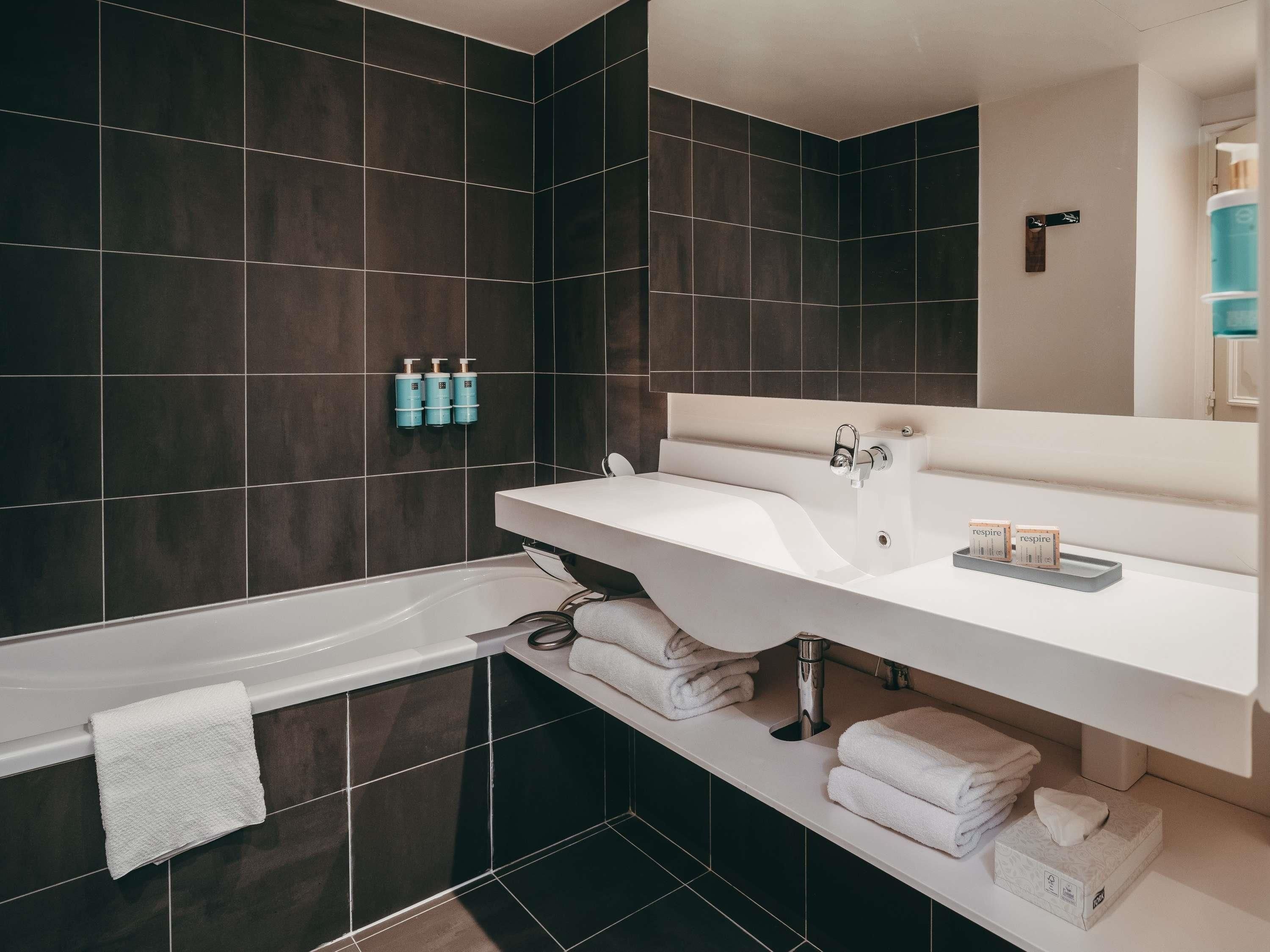 Un baño moderno con baldosas oscuras, un lavabo blanco y una bañera.