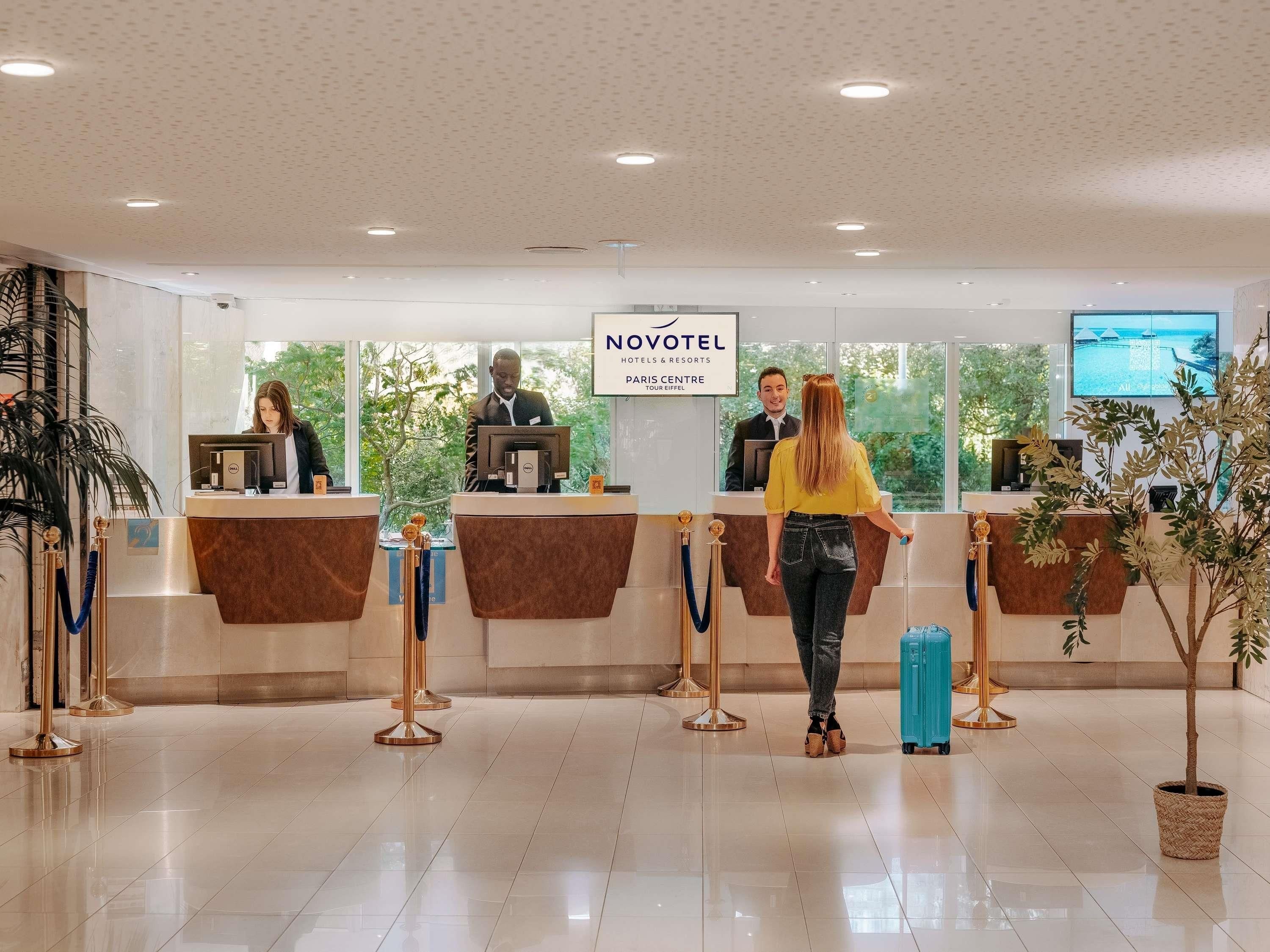 A hotel reception area with a reception desk, a digital screen, and a view of the outdoors.