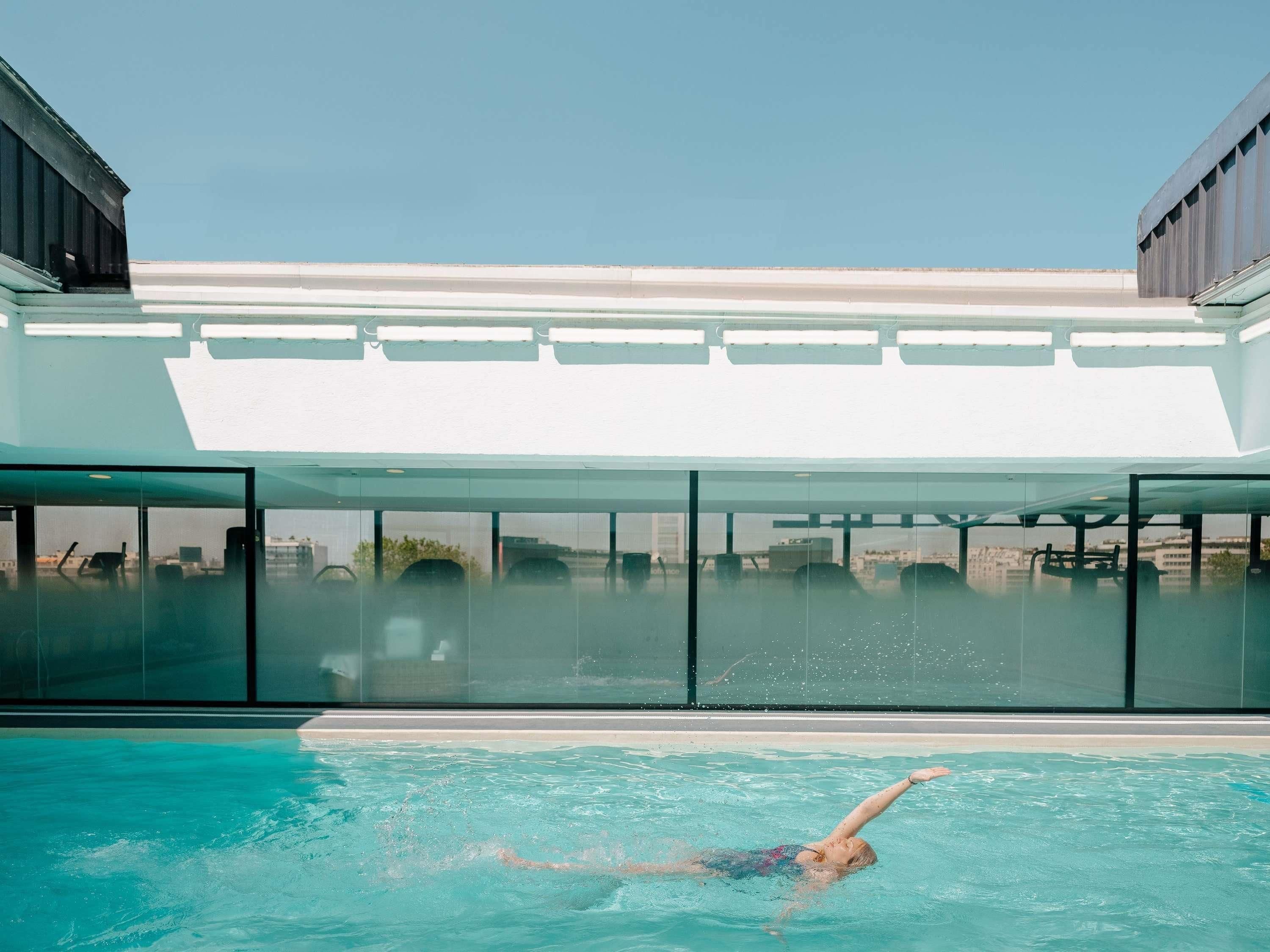 Ein Schwimmbecken mit einer schwimmenden Person, großen Fenstern und einem modernen Gebäudebau.
