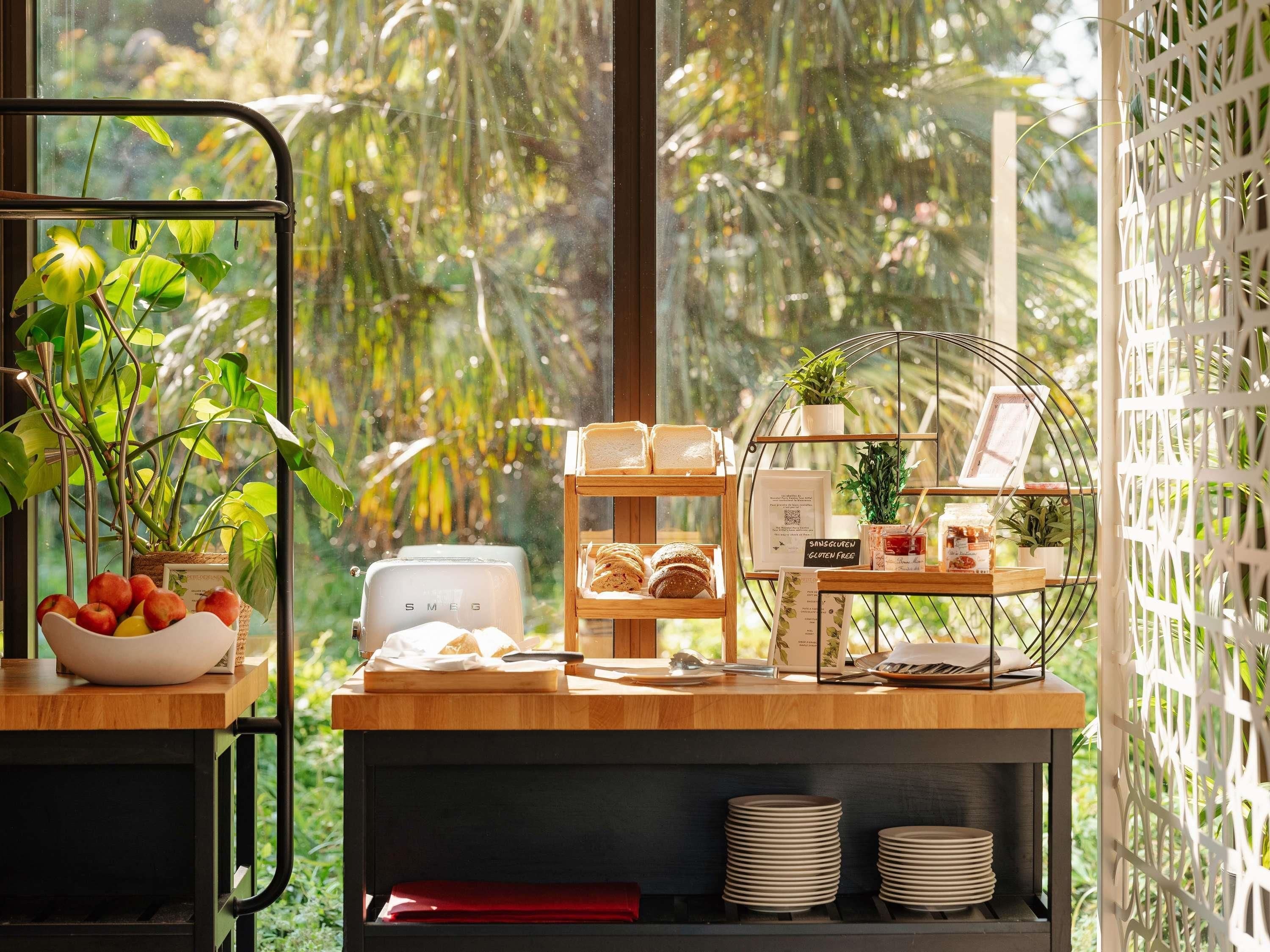 Un comptoir de petit-déjeuner avec un grille-pain, un saladier de fruits, une plante et un tableau affichant le menu.
