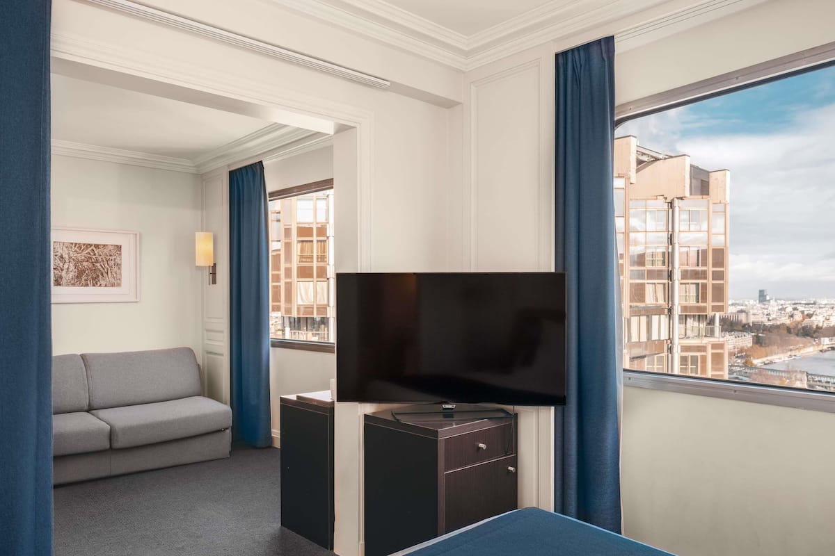 Habitación de hotel con cama, televisión, escritorio, sofá y ventana con vista a la ciudad.
