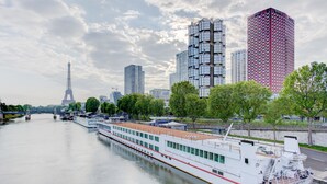 A river cruise ship docked near a city with modern buildings and the Eiffel Tower in the background. - Novotel Paris Centre Tour Eiffel (Paris)