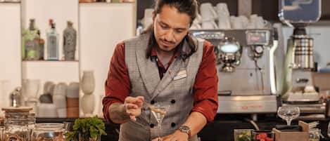 A bartender at a bar with a coffee machine and various bottles in the background.