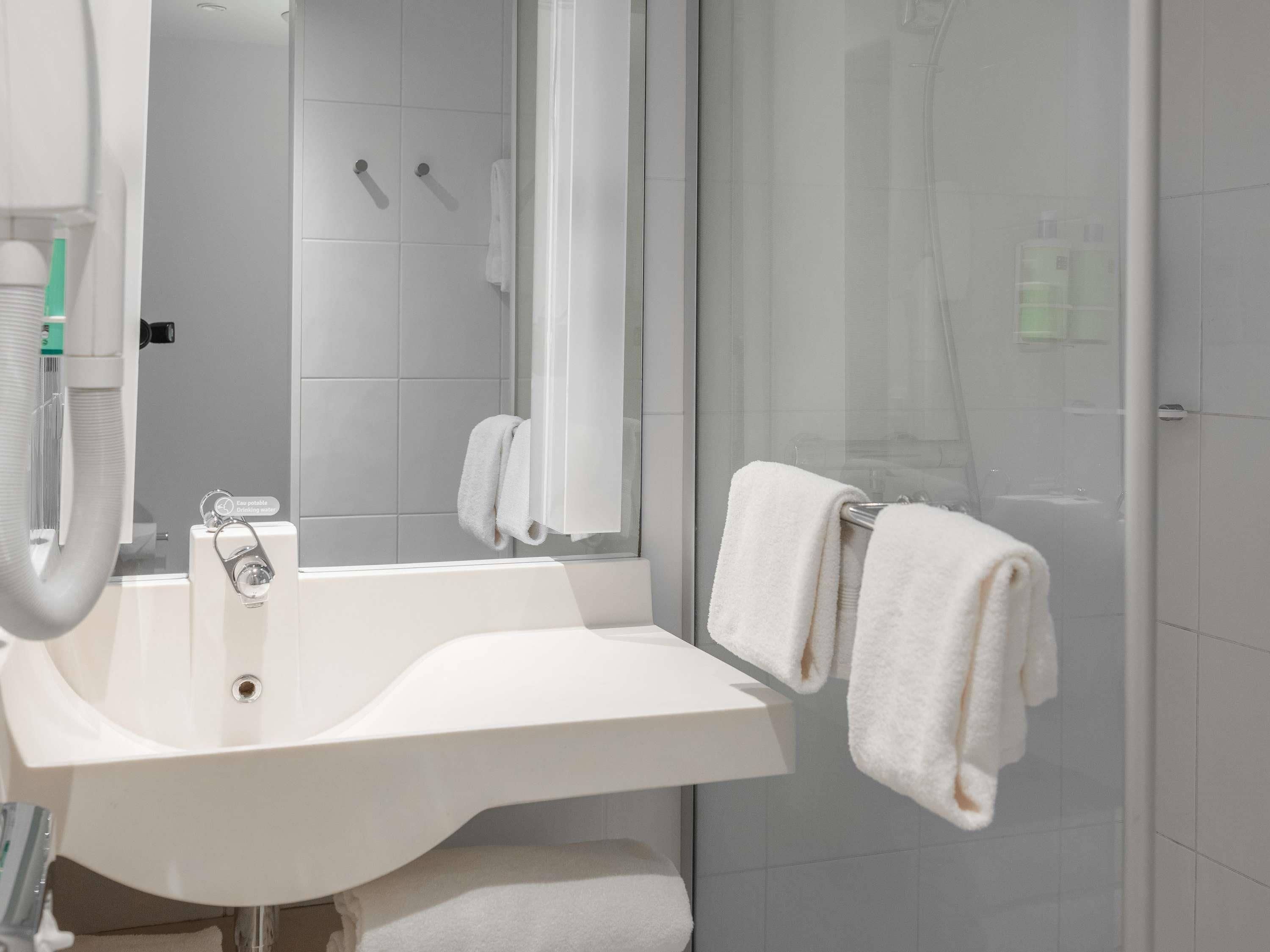 A modern bathroom with a white sink, mirror, and towel rack.