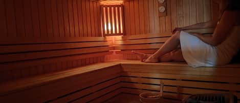 A person sitting on a wooden bench in a sauna with a small window and a clock on the wall.