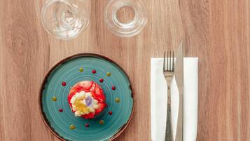 Une assiette turquoise sur laquelle repose un dessert, une fourchette et un couteau posés sur une serviette, et deux verres vides sur une table en bois.
