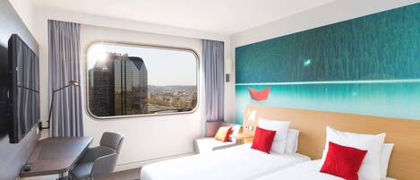 Habitación de hotel con cama, escritorio, silla y ventana con vista a la ciudad.