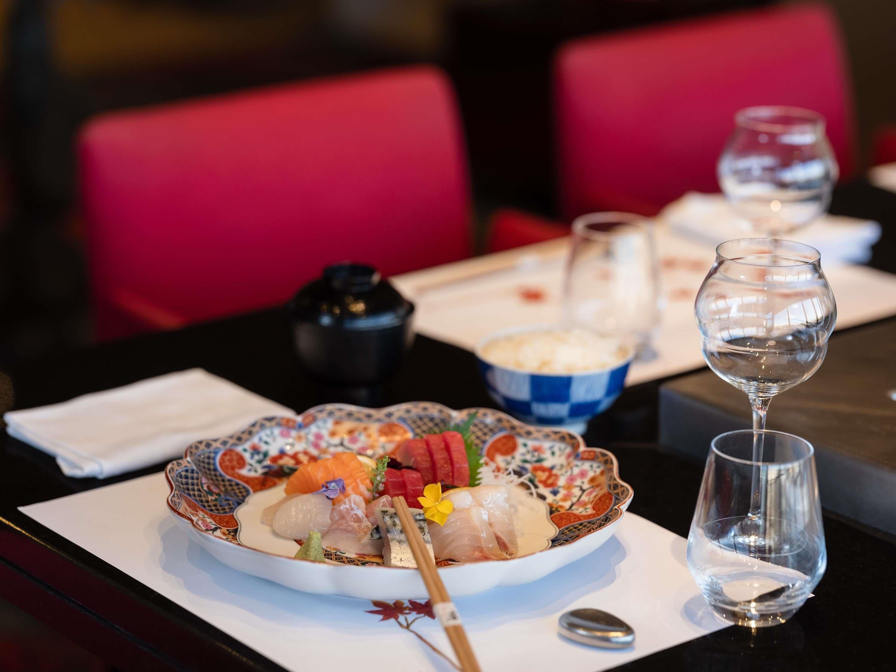 A table with a plate of sashimi, a bowl of rice, and a glass of water.