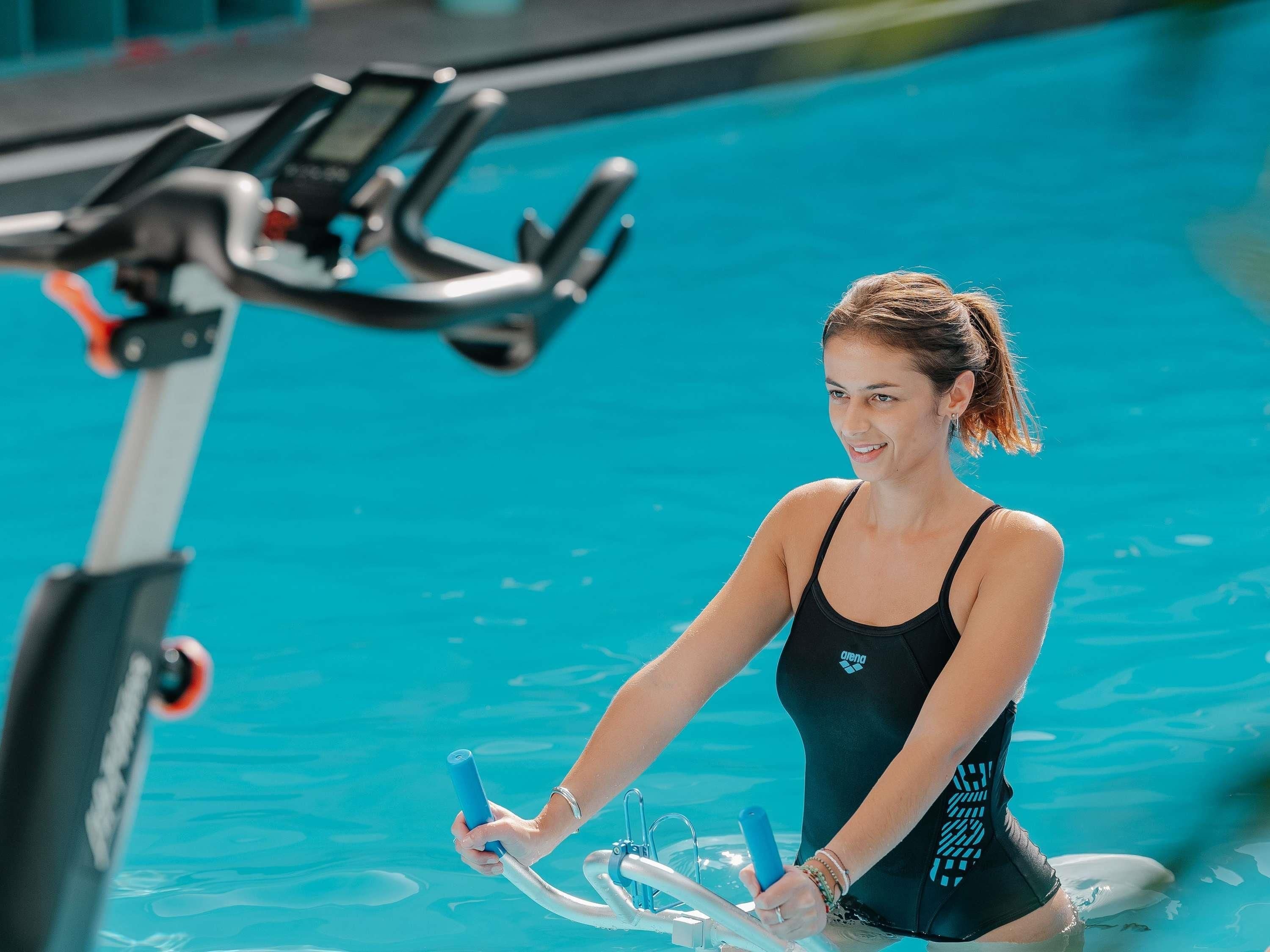 Une personne portant un maillot de bain noir et utilisant un tapis roulant aquatique dans une piscine.