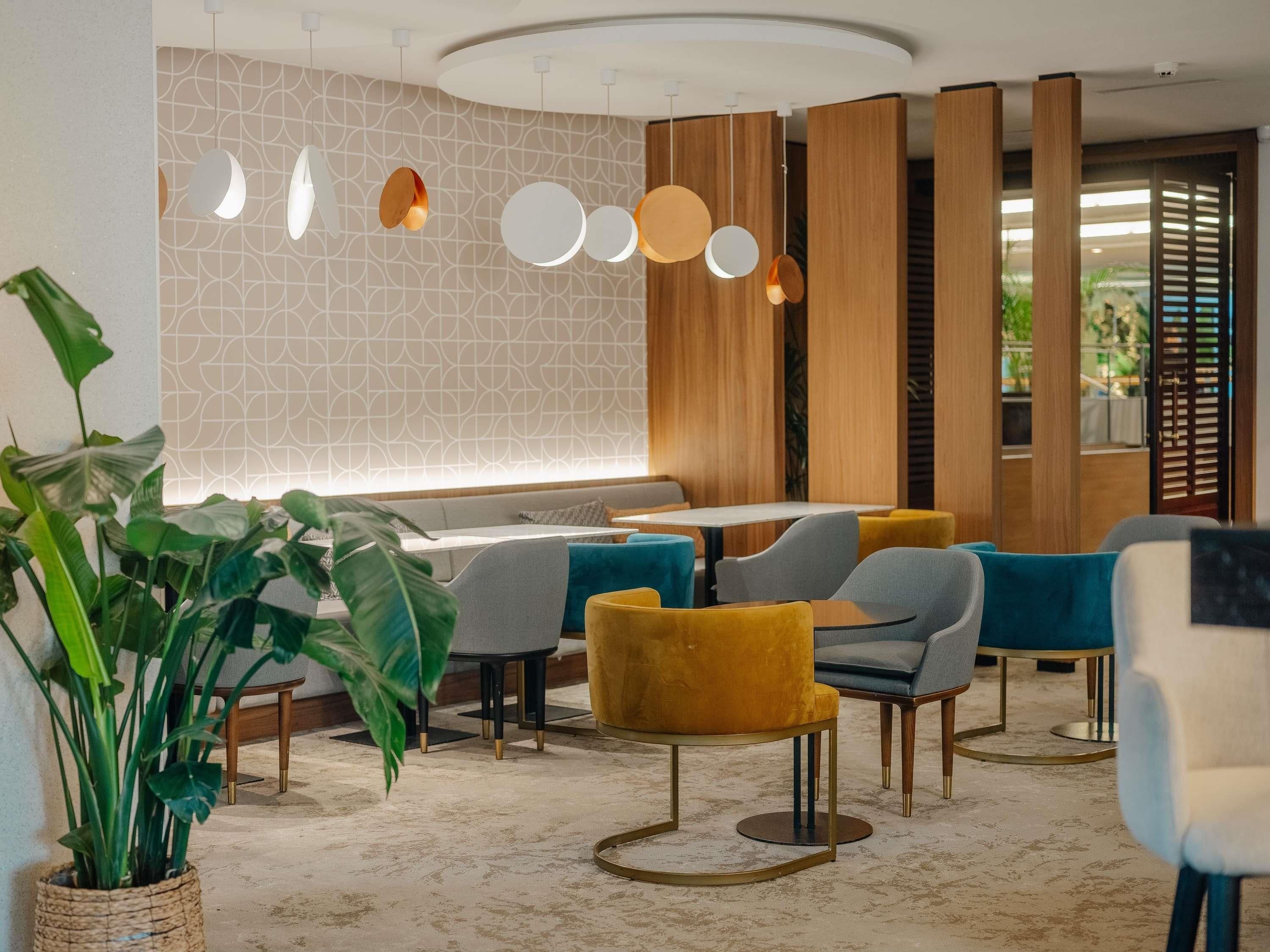 A modern interior with a seating area, tables, hanging pendant lights, and a patterned wall.