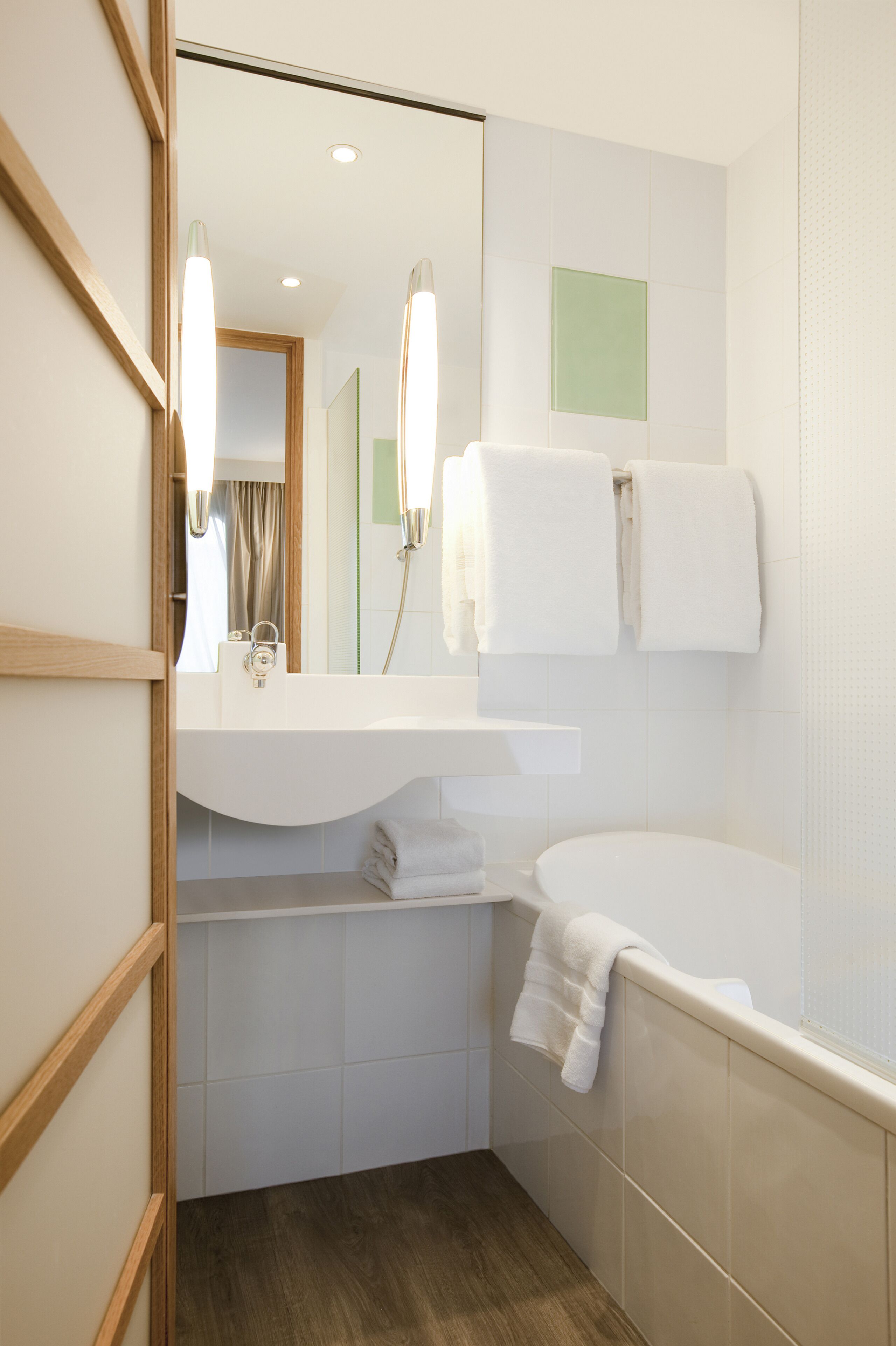 A modern bathroom with a wooden-framed mirror, a white sink, a bathtub, and a towel rack.