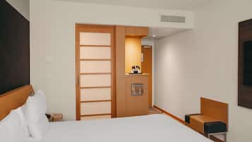 A hotel room with a bed, a wooden wardrobe, a small desk with a chair, and a wall-mounted TV.