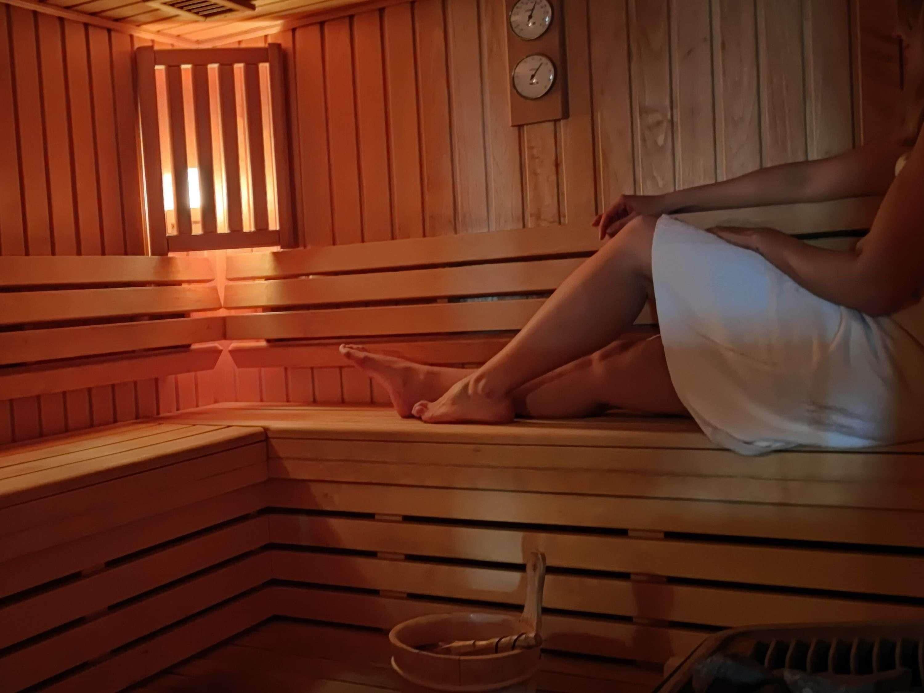 Un sauna avec des bancs en bois, un mur en bois orné d’une horloge et un petit bol posé sur le sol.