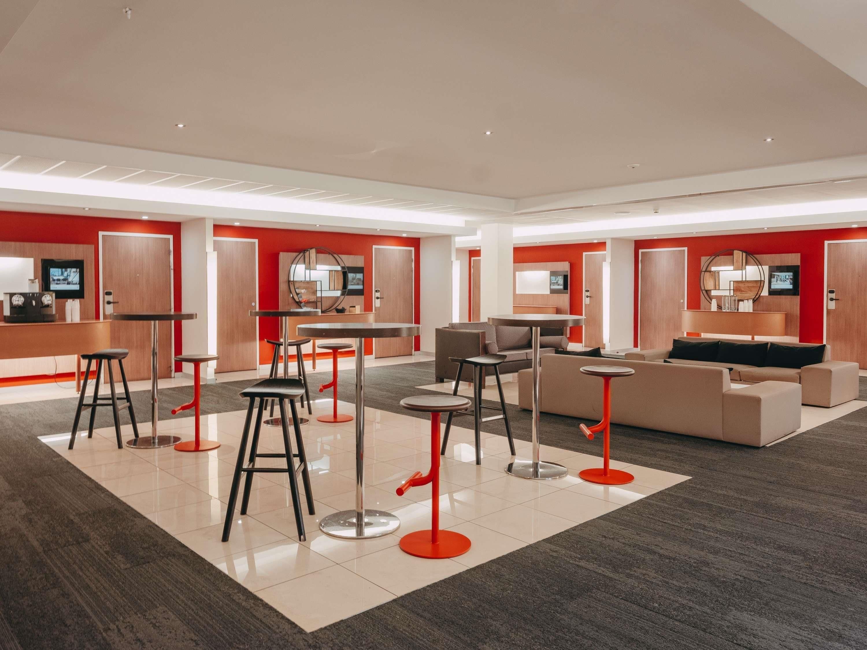 Un hall d’hôtel moderne avec un comptoir d’accueil, un espace salon et un grand miroir.
