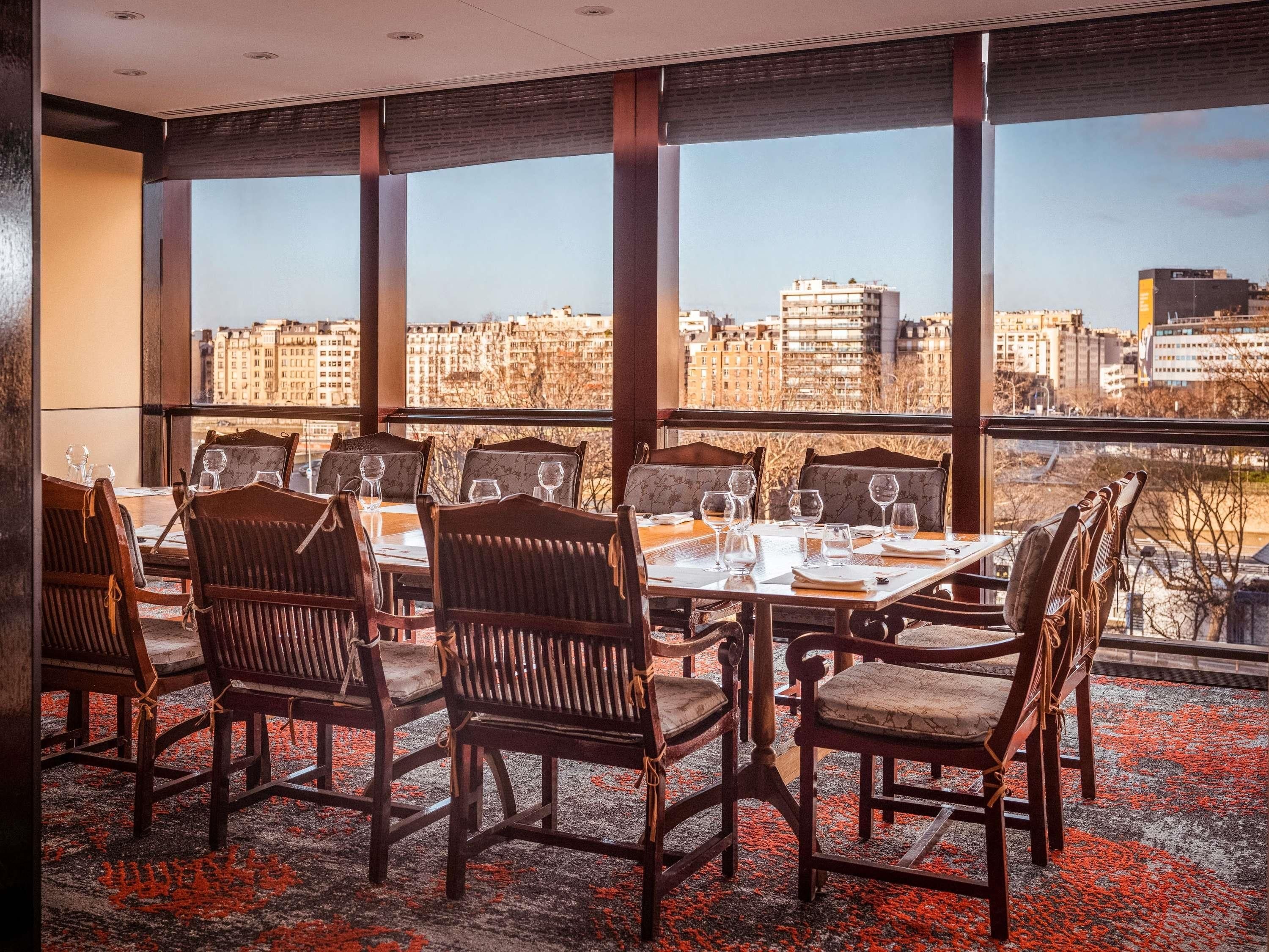 A dining area with tables and chairs, large windows, and a city view.