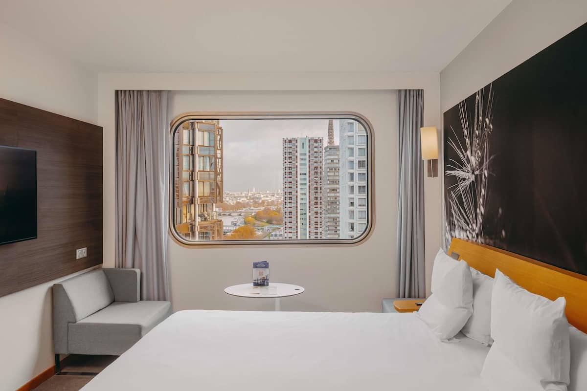 Habitación de hotel con una cama grande, un televisor en la pared, una mesita y vistas a edificios altos.