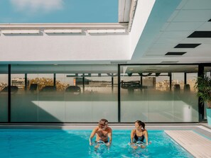 Una piscina interior moderna con paredes de vidrio transparente, vistas a la ciudad y un diseño arquitectónico contemporáneo.