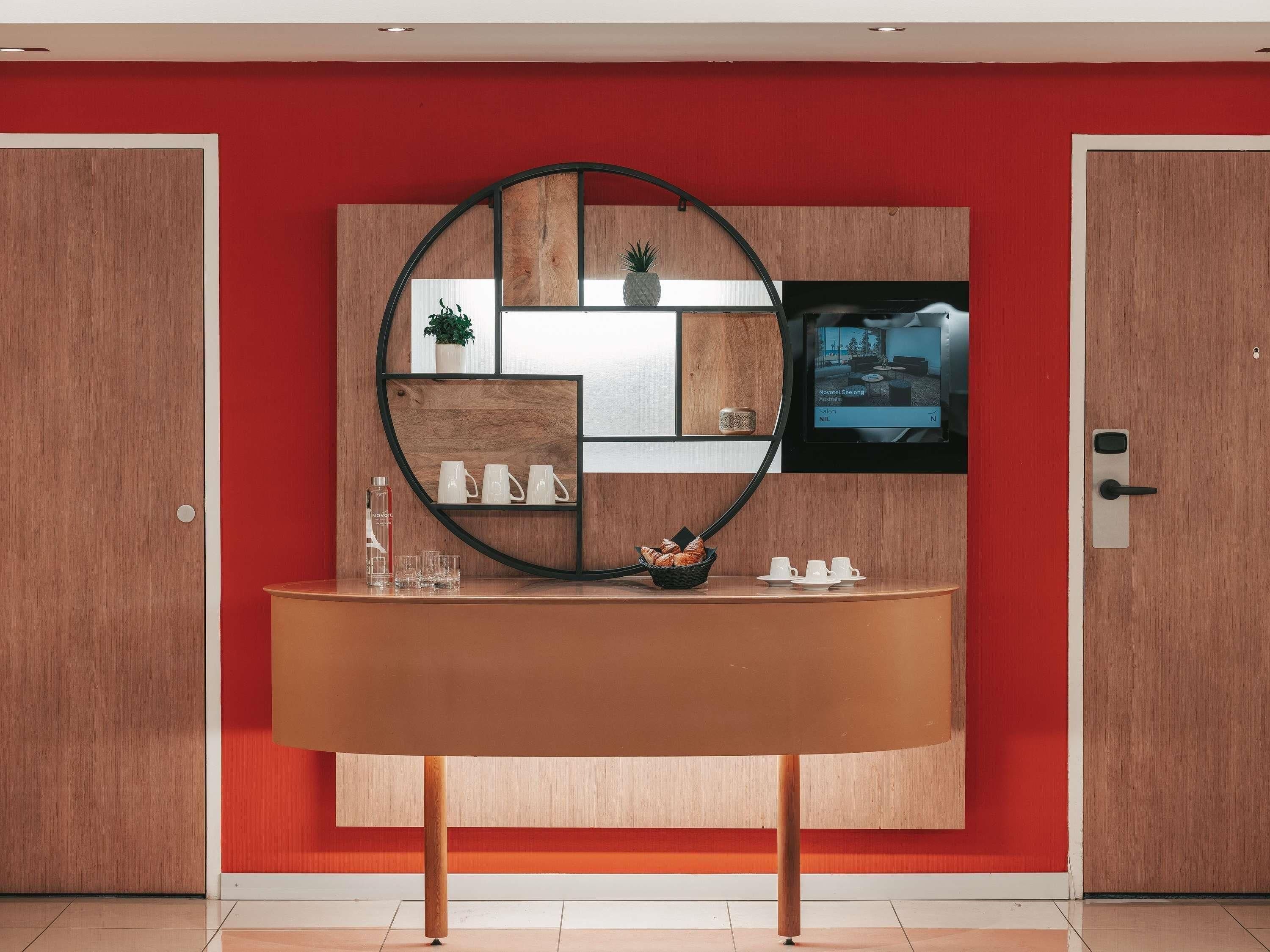 A reception desk with a wooden finish, a circular mirror, and a television screen displaying a room.