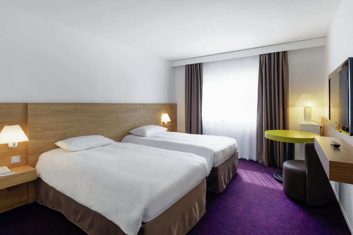 Une chambre d’hôtel avec deux lits, un bureau, une chaise, une table ronde et un miroir.