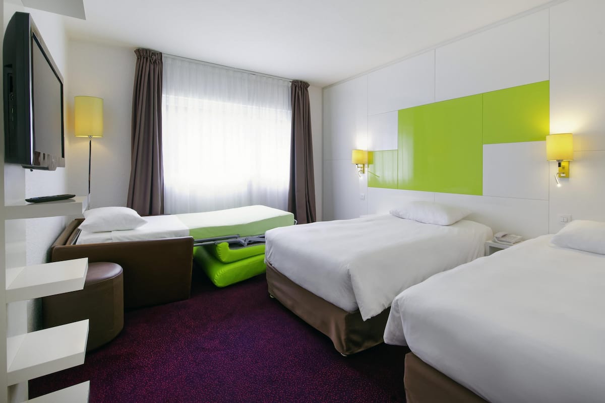 Une chambre d’hôtel avec deux lits, un bureau, une chaise, une télévision et une fenêtre avec des rideaux.