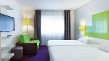 A hotel room with a bed, a chair, a TV, a lamp, and a window with curtains.