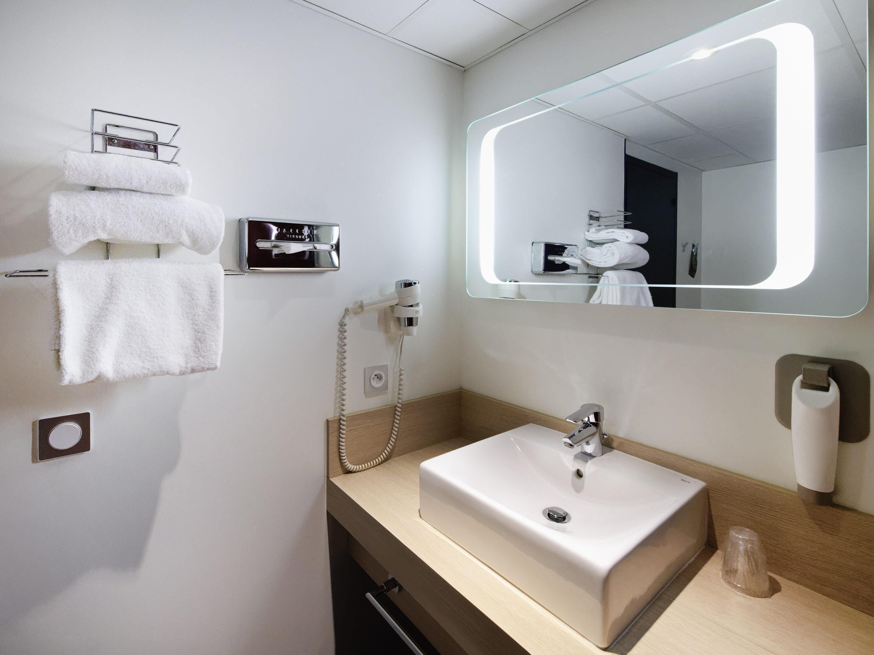 Un bany modern amb un lavabo, penjador de tovalloles i un mirall amb il·luminació integrada.