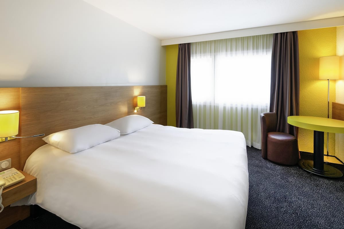 Une chambre d’hôtel avec un grand lit, une lampe de chevet, une petite table et une chaise.