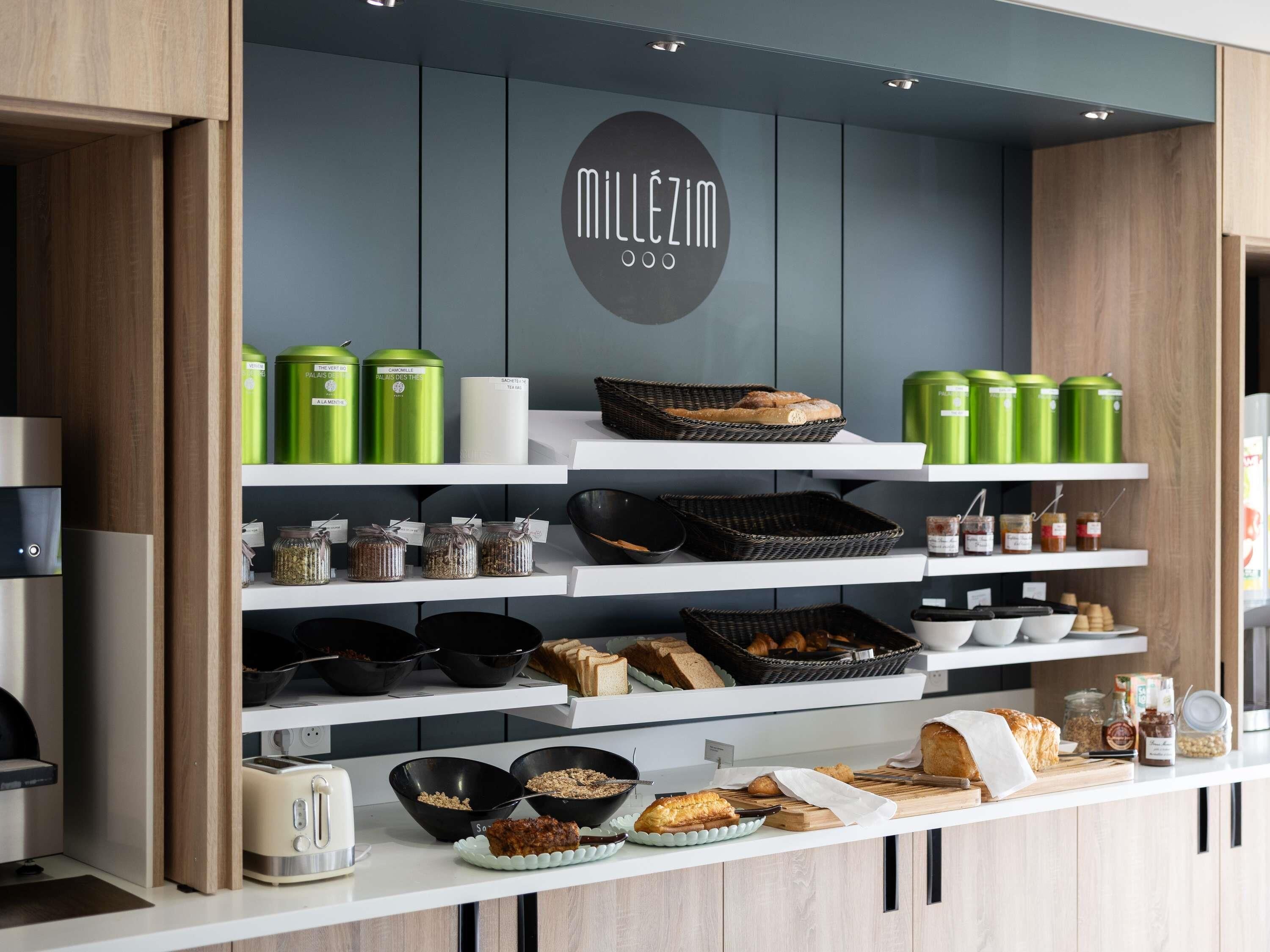 A kitchenette with a coffee machine, tea kettle, and various food items on shelves.