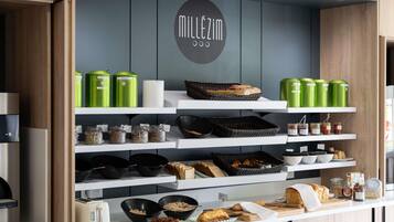 A kitchenette with a coffee machine, tea kettle, and various food items on shelves.