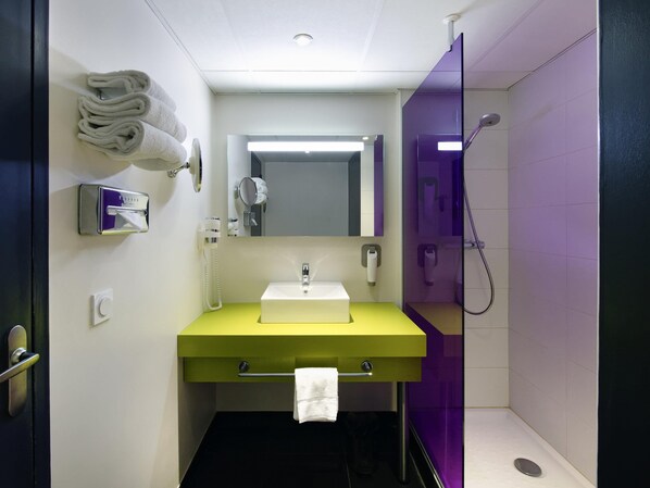 A bathroom with a yellow sink, a mirror, a towel dispenser, and a shower.