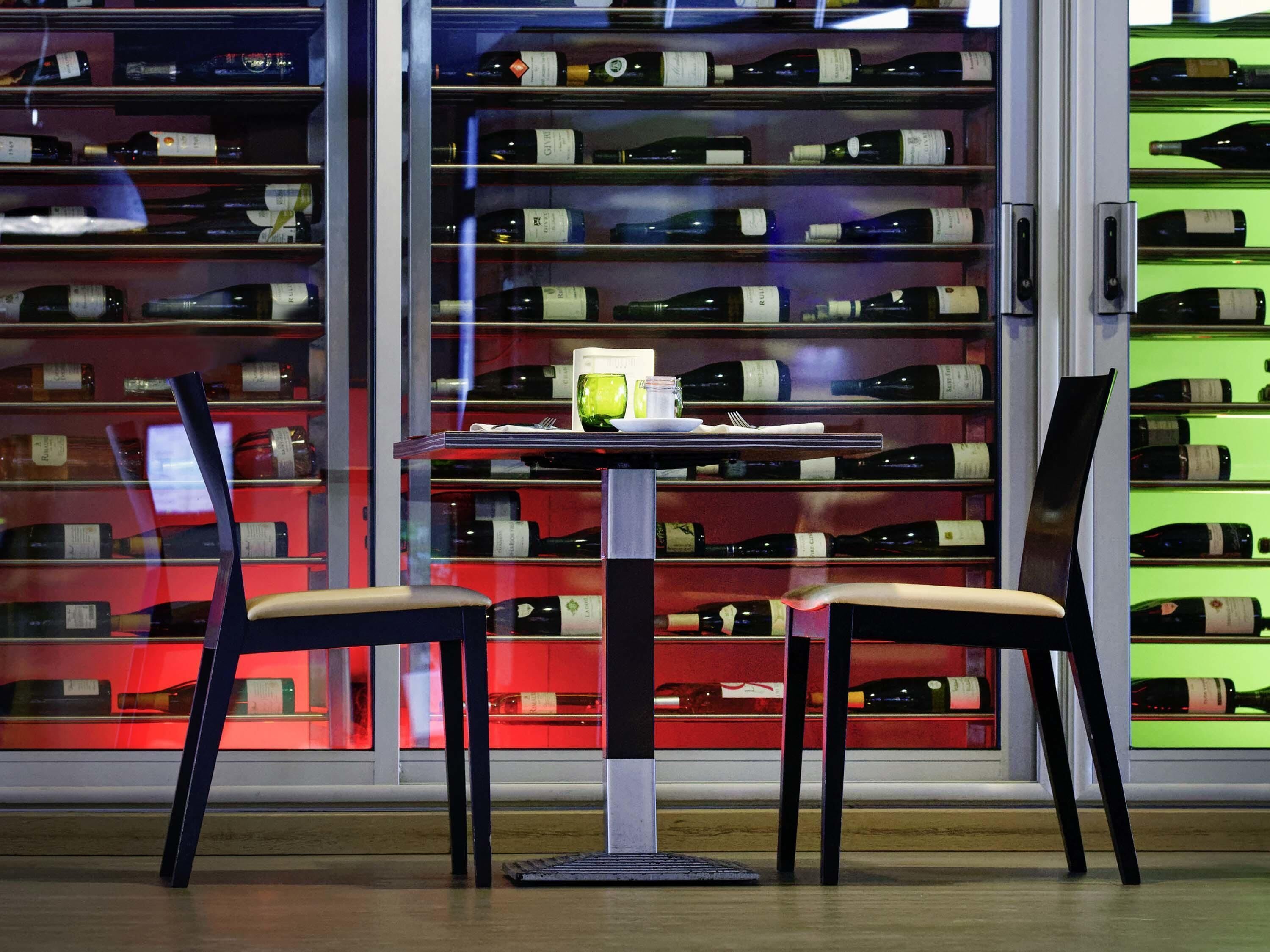 A wine rack with bottles, a table with a glass, and two chairs.