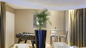 A modern room with a foosball table, a large potted plant, and two glass-top tables with chairs. - Ibis Styles Chalon sur Saone (Chalon-sur-Saone)
