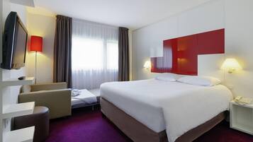 A hotel room with a bed, a desk, a chair, a TV, and a window with curtains.