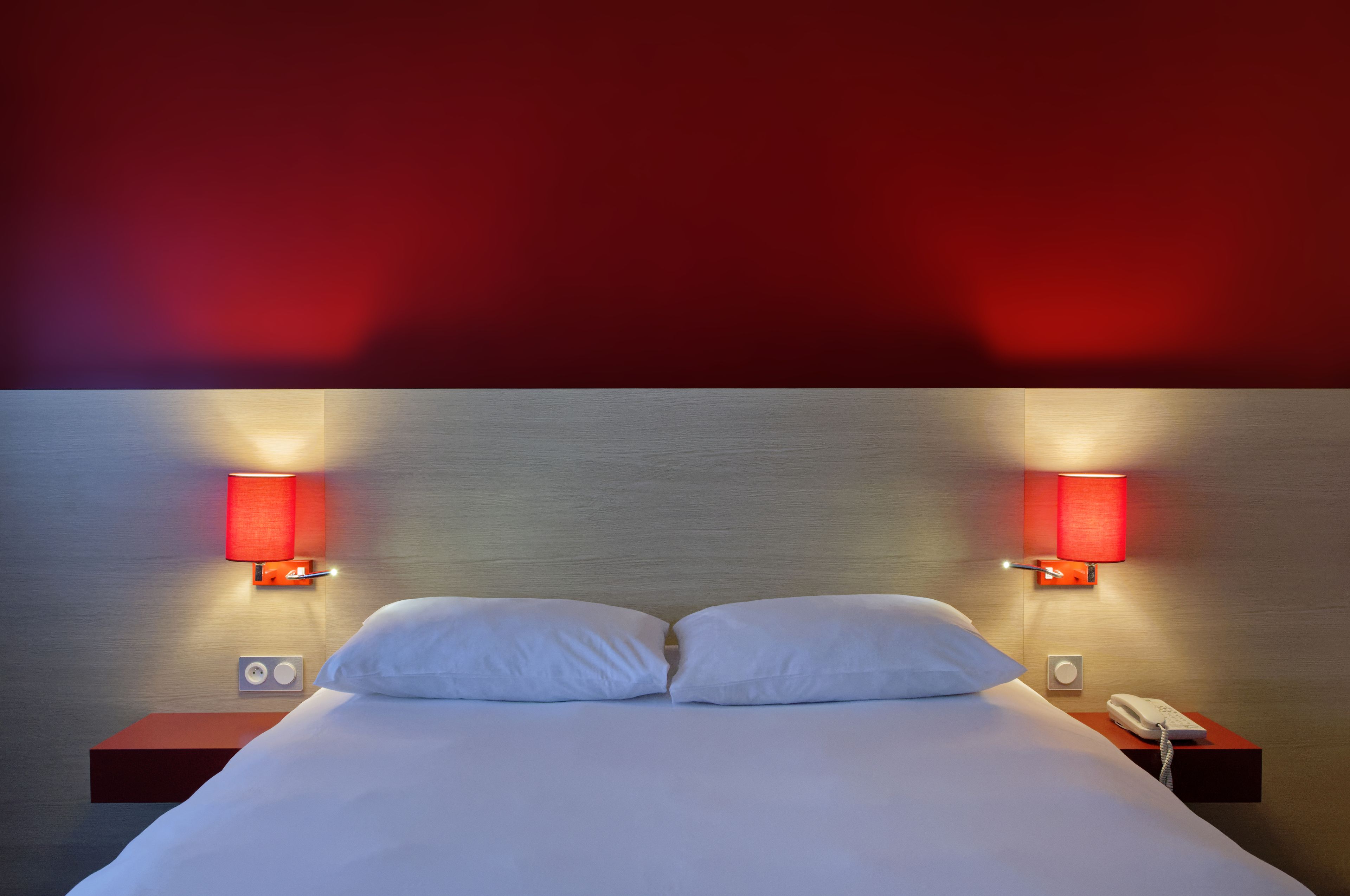 Et hotelværelse med en pænt redt seng, to sengeborde, en vægmonteret lampe og en telefon.