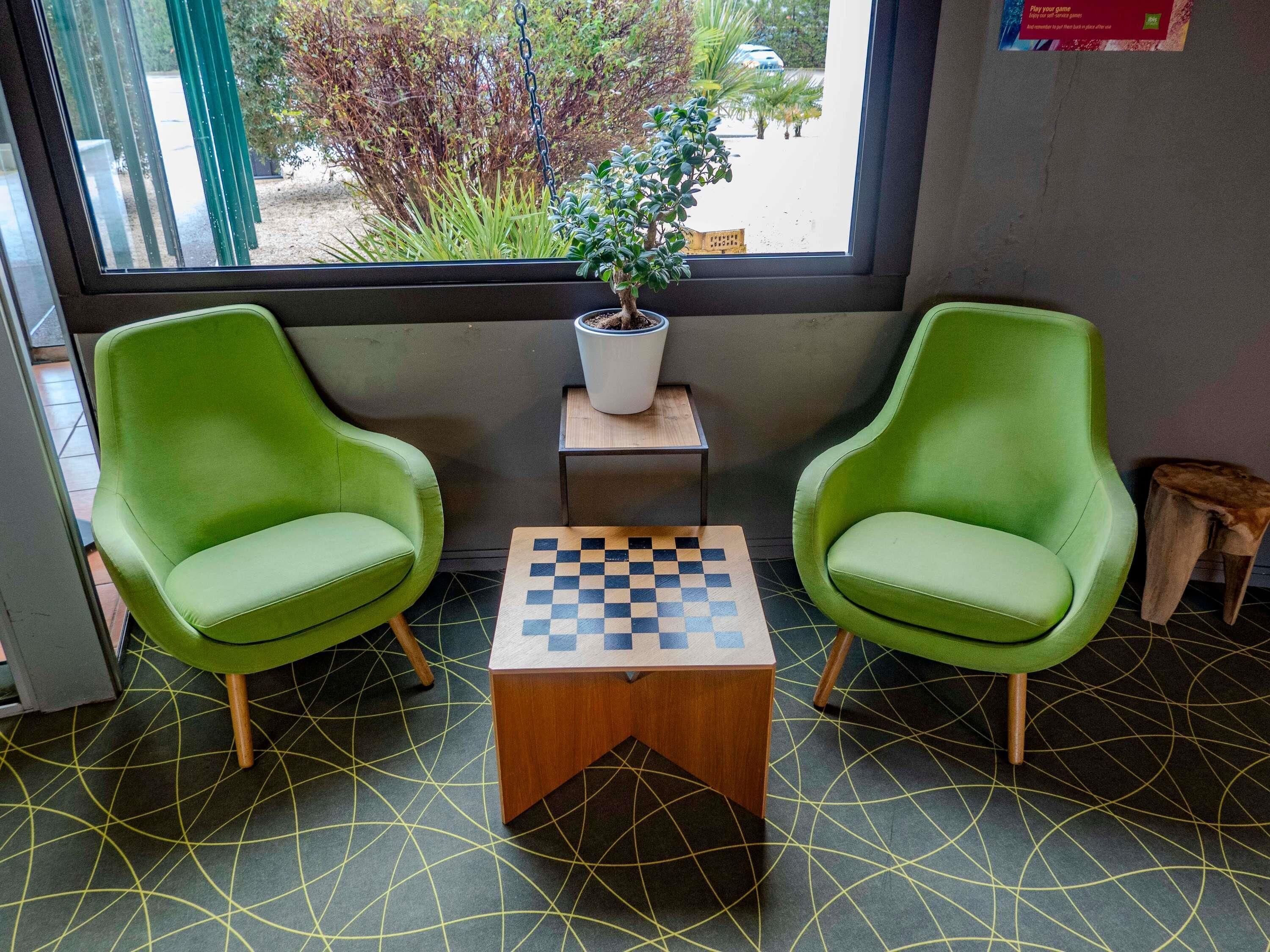 Deux chaises vertes, une petite table avec un jeu d’échecs et une plante en pot posée sur une autre petite table.