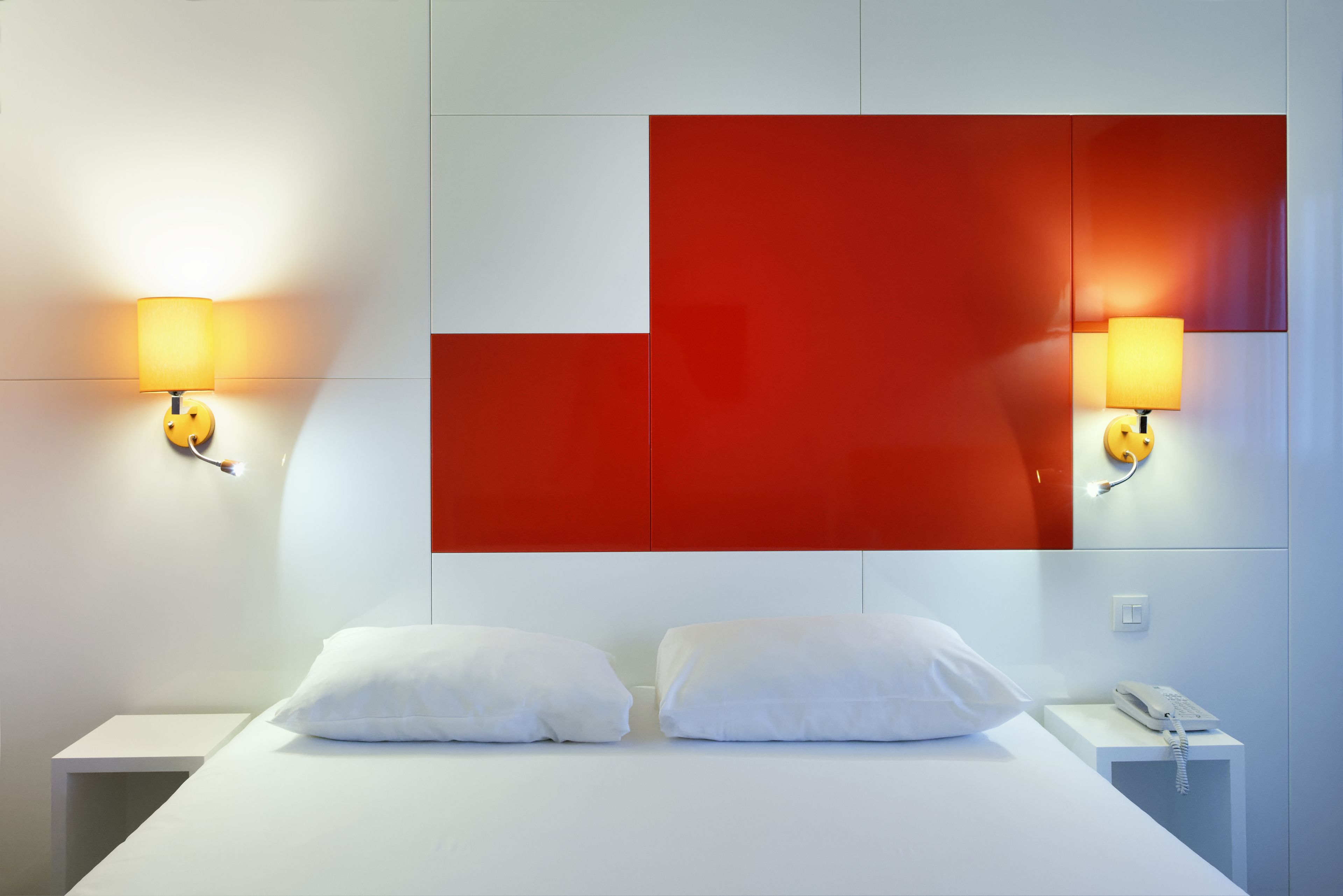 A hotel room with a bed, two bedside tables, and a wall-mounted red panel.